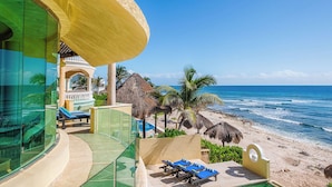 Un hotel frente a la playa con piscina infinita de cristal, sillas de descanso en la orilla y vistas al océano.