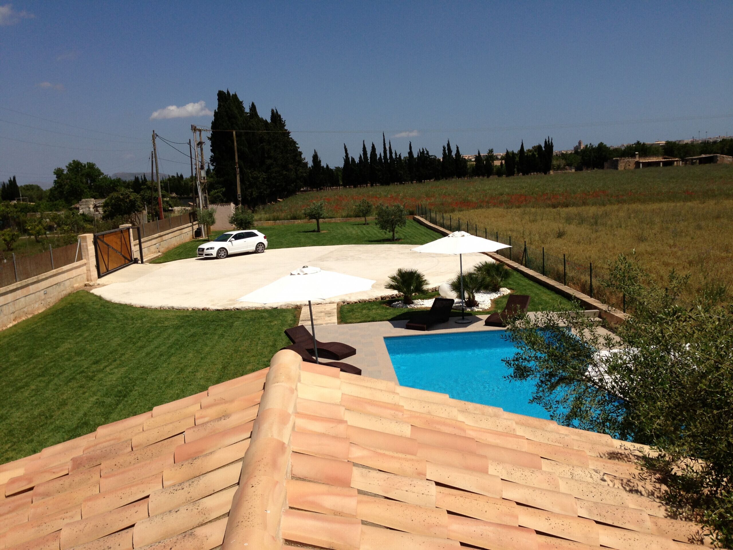 A backyard with a swimming pool, a white car, and a patio area with umbrellas.