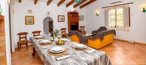 A dining area with a long table set for a meal, a sofa, and a television in the background.