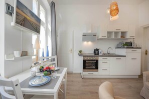 Eine moderne Küche mit weißen Schränken, ein Essbereich mit Tisch für Zwei und eine Wohnbereich mit Sofa.