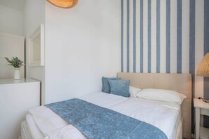 Ein Schlafzimmer mit einem Bett, einem Nachttisch, einer Lampe, einem Spiegel und einer Wand mit vertikalen Streifen.