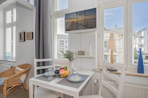 Ein Zimmer mit einem weißen Tisch, einem Korbstuhl und Blick auf einen Steg durch ein Fenster.