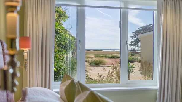 A bedroom with a large window offering a view of a garden and a building. - Marsh Lodge, Aldeburgh (Aldeburgh)