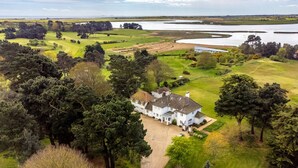 A large white house with a spacious driveway, surrounded by lush greenery and a golf course. - Marsh Lodge, Aldeburgh (Aldeburgh)