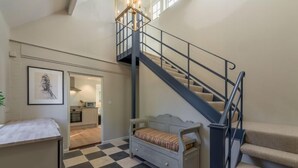 A spacious room with a checkered floor, a bed, a staircase, and a kitchen area visible through an open door. - Marsh Lodge, Aldeburgh (Aldeburgh)