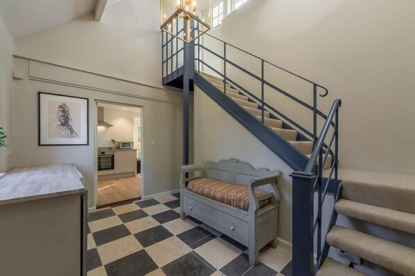 A spacious room with a checkered floor, a bed, a staircase, and a kitchen area visible through an open door.