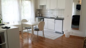 A compact kitchen with white cabinets, a dining table with two chairs, a built-in oven, and a small refrigerator. - FeWo II, V und VI  - Altstadt - Am grossen Garten (Dresden)