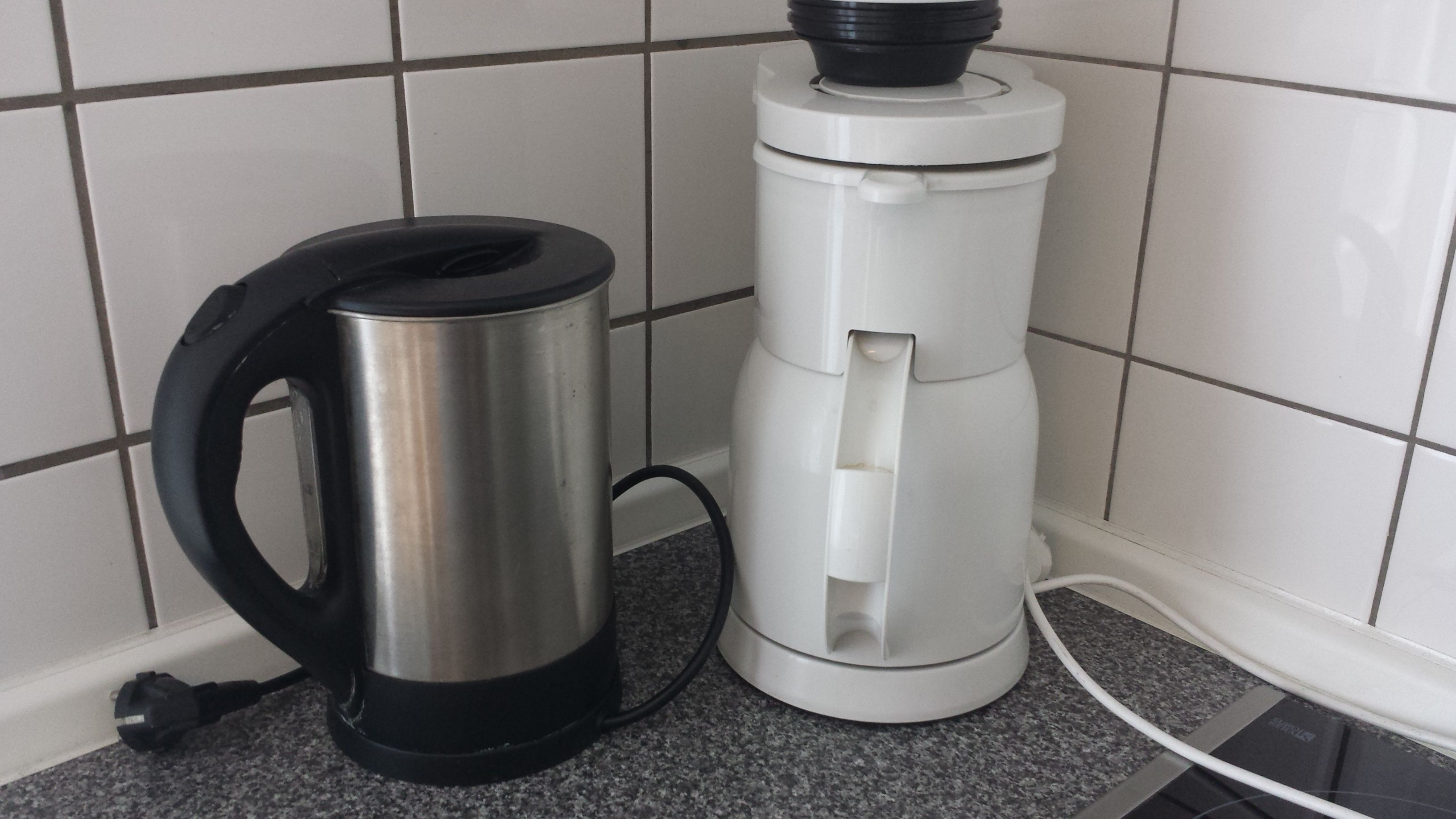 Een keuken met een RVS-kettle en een witte elektrische kettle op een granieten aanrecht.