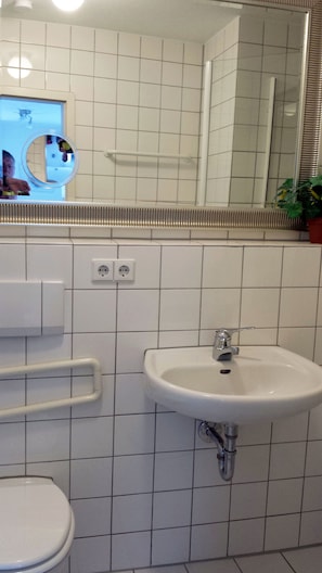 A bathroom with a white tiled wall, a sink with a chrome faucet, a mirror, and a toilet. - FeWo II, V und VI  - Altstadt - Am grossen Garten (Dresden)