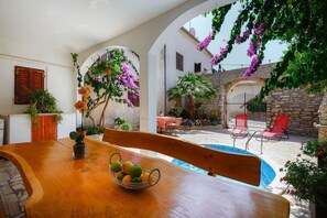 A wooden table with a fruit bowl, a pool, red chairs, and a stone wall in a sunny outdoor setting. - Just 700 meters to sandy beach with pool (Medulin)
