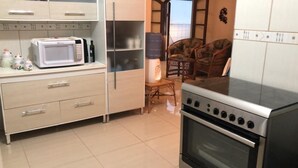 A kitchen with a microwave, refrigerator, stove, and a water dispenser. There is a wicker chair and a small table in the background. - Beira Mar House with pool and waterfall in Mongaguá with 06 suites (Mongaguá)