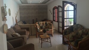 A living room with sofas, a coffee table, and a large window with a view. - Beira Mar House with pool and waterfall in Mongaguá with 06 suites (Mongaguá)