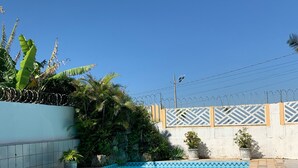 A swimming pool with a tiled deck, surrounded by a low wall with barbed wire. - Beira Mar House with pool and waterfall in Mongaguá with 06 suites (Mongaguá)