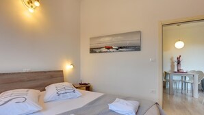 Quarto moderno com uma cama grande, um quadro na parede e uma área de refeições visível através de uma porta aberta.