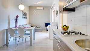 Cozinha moderna com armários brancos, fogão a gás e área de refeições com mesa e cadeiras brancas.