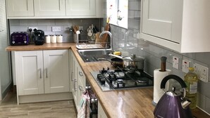 A modern kitchen with white cabinets, a gas stove, a kettle, and various kitchen utensils. - The Woodfarm Lodge - 3 Bedroom House (Oxford)
