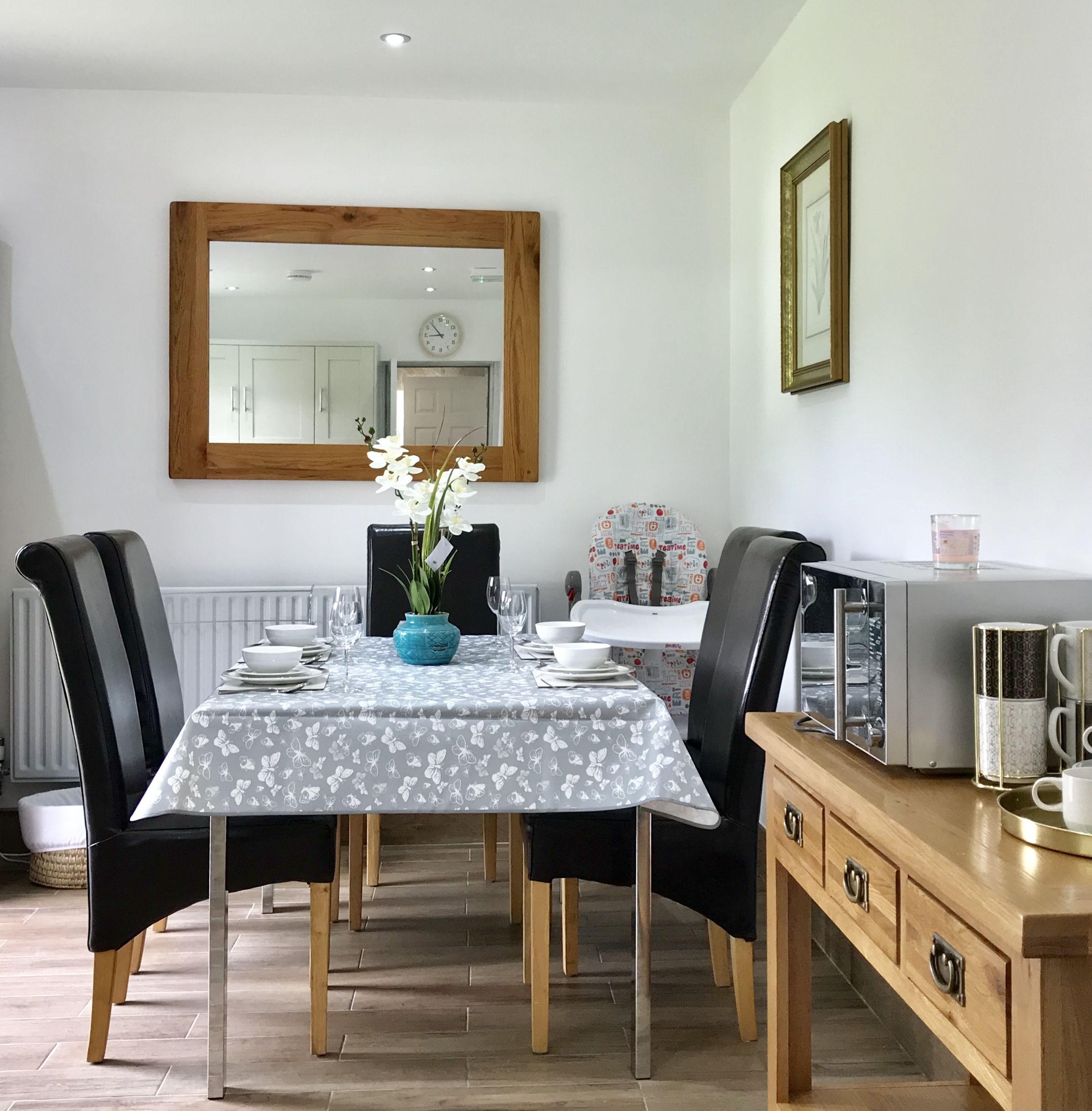 A dining area with a table set for four, a blue vase with flowers, and a wooden cabinet with drawers.