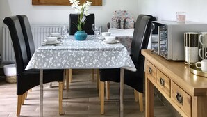 A dining area with a table set for four, a blue vase with flowers, and a wooden cabinet with drawers. - The Woodfarm Lodge - 3 Bedroom House (Oxford)