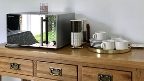 A kitchen area with a modern microwave, a coffee maker, and a stack of white cups on a wooden cabinet. - The Woodfarm Lodge - 3 Bedroom House (Oxford)