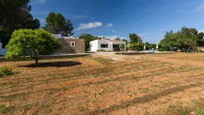 A white building with a small porch, surrounded by a grassy area and trees. - CANA LALI (Santa Eulalia del Río)