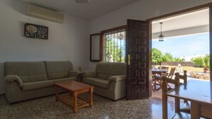 A living room with a sofa, a coffee table, and a dining area with a table and chairs. There is a window with decorative iron bars and a view of the outdoors. - CANA LALI (Santa Eulalia del Río)
