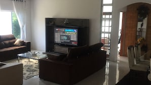 Un salon moderne avec un téléviseur à écran plat, un canapé marron, une table basse en verre et un tapis à motifs.