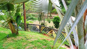 Une vue depuis un espace abrité, doté d’une balustrade en bois, donnant sur une zone herbeuse et un plan d’eau.