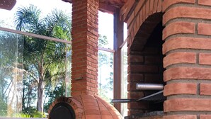 Un four en briques installé à l’extérieur, doté d’une cheminée, ainsi qu’une poubelle et une pile de bois à proximité.