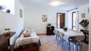 Een knus, goed verlichte kamer met een bed, een tafel met stoelen, een televisie en een raam met gordijnen.
