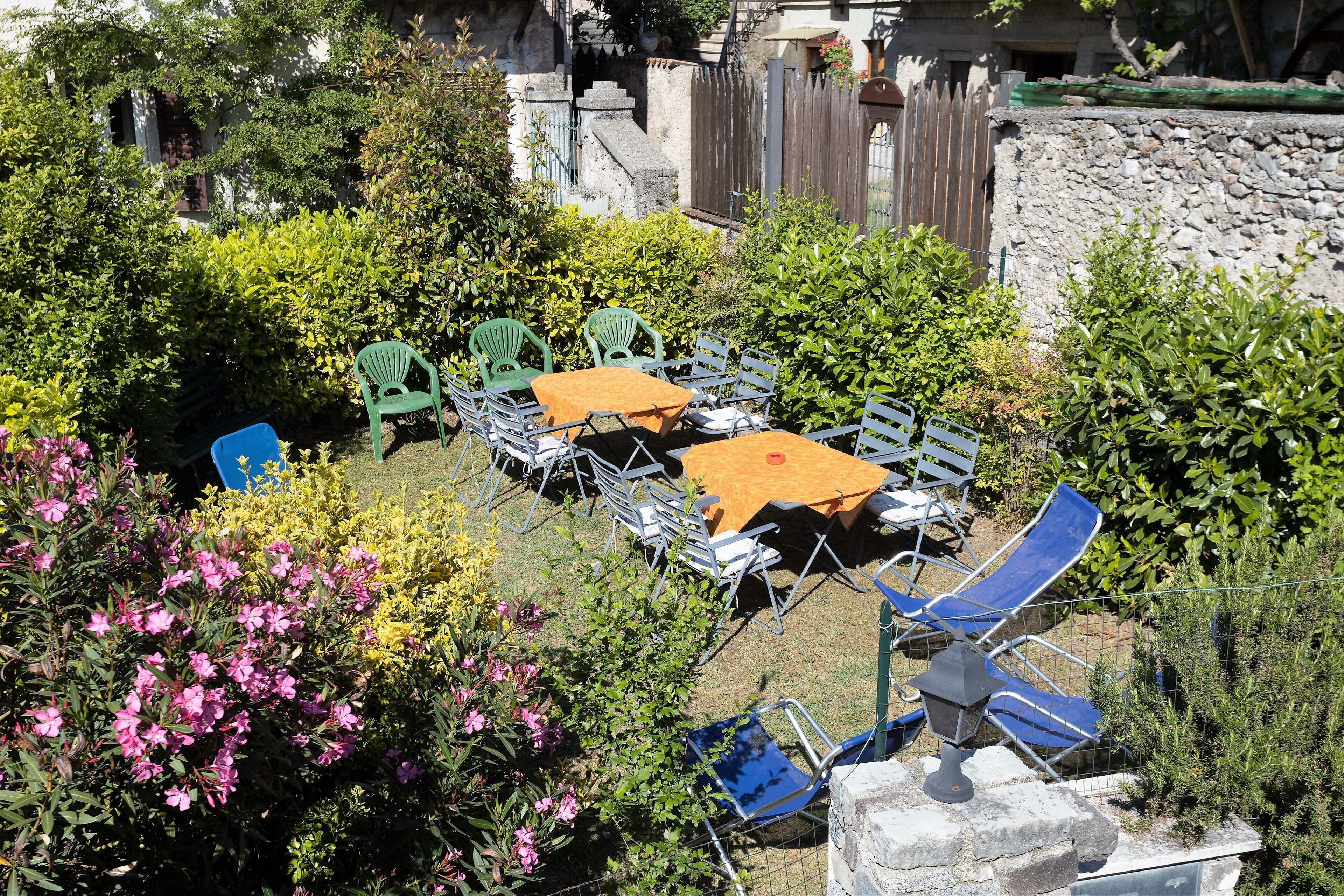 Un espace extérieur aménagé en terrasse, avec des tables et des chaises, entouré d’une végétation luxuriante et d’un mur en pierre.