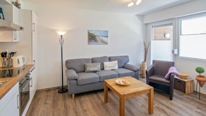 A modern living room with a grey sofa, a wooden coffee table, a floor lamp, and a small potted plant. - Vacation apartment Strandbox (Norddeich)