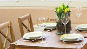 A wooden dining table set with plates, cutlery, and wine glasses, with a glass vase containing yellow flowers in the center. - Vacation apartment Strandbox (Norddeich)