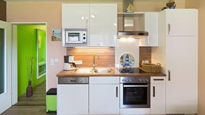 A compact kitchen with white cabinets, a microwave, a stove, and a sink. - Vacation apartment Strandbox (Norddeich)