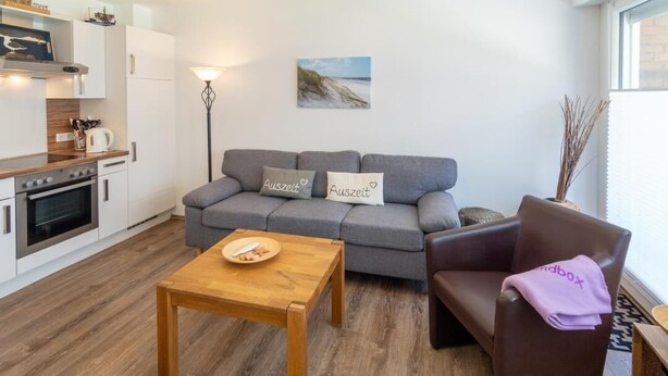 A modern living room with a grey sofa, a wooden coffee table, and a brown leather chair. - Vacation apartment Strandbox (Norddeich)