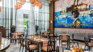 Un restaurante con mesas redondas, lámparas colgantes de mimbre y un mural en la pared.