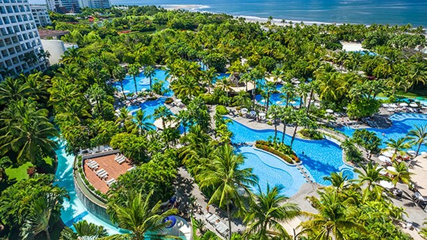 Un resort con múltiples piscinas rodeado de exuberante vegetación y palmeras, con vista a una playa y el océano.