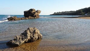 A beach with clear shallow waters and rocky formations.