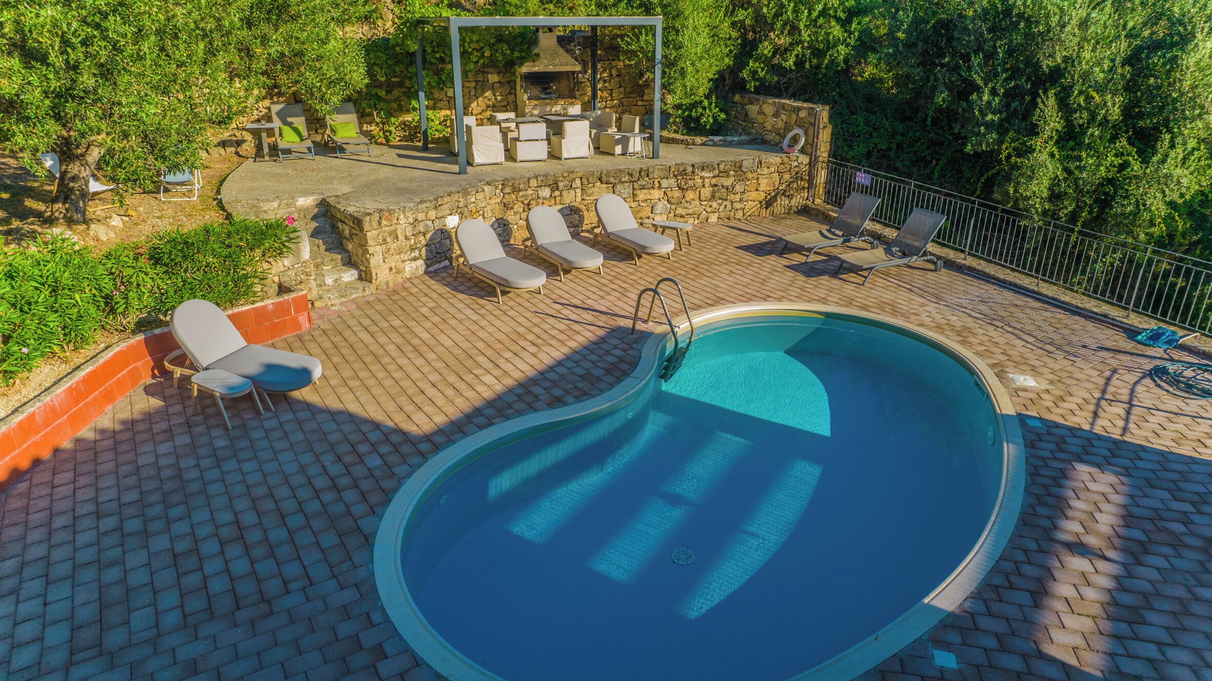 Ein Swimmingpool mit Liegestühlen und Grillplatz.