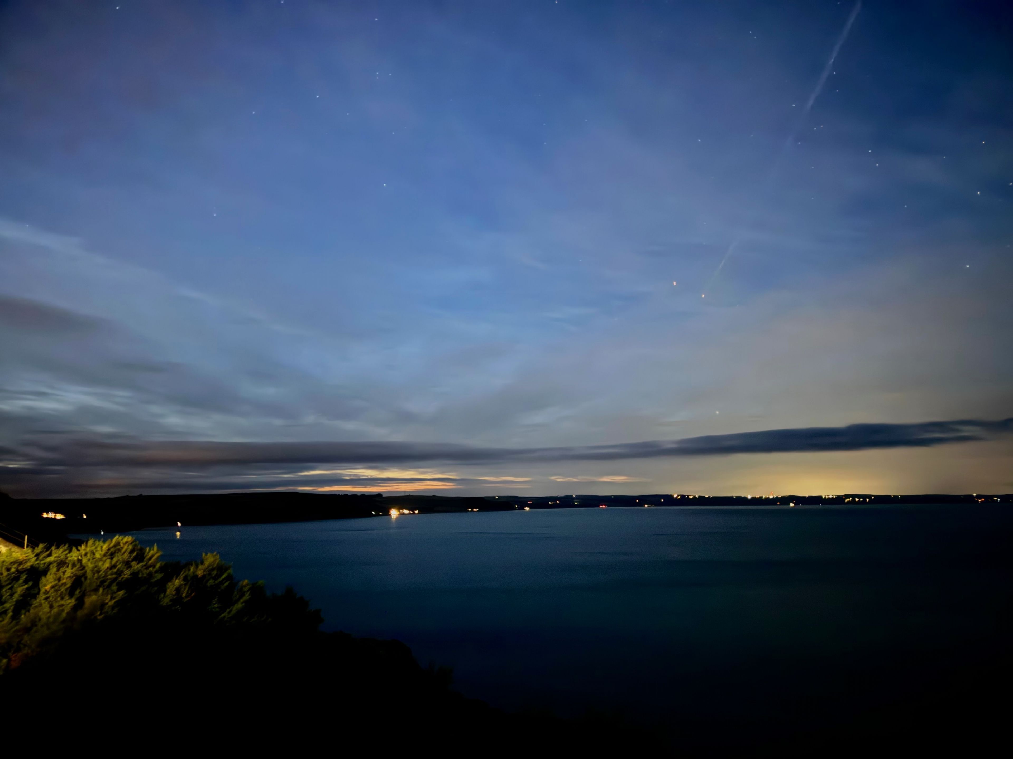 En nattlig vy över en stilla vattenyta med en klar himmel och avlägsna stadsljus.