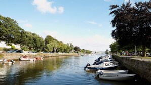 Ein Kanal mit am rechten Ufer vertäuten Booten, gesäumt von Bäumen und einer Steinmauer.