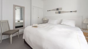 Ein ordentlich eingerichtetes Schlafzimmer mit einem großen Bett, einem Nachttisch, einem Stuhl, einer Nachttischlampe und einem Spiegel.