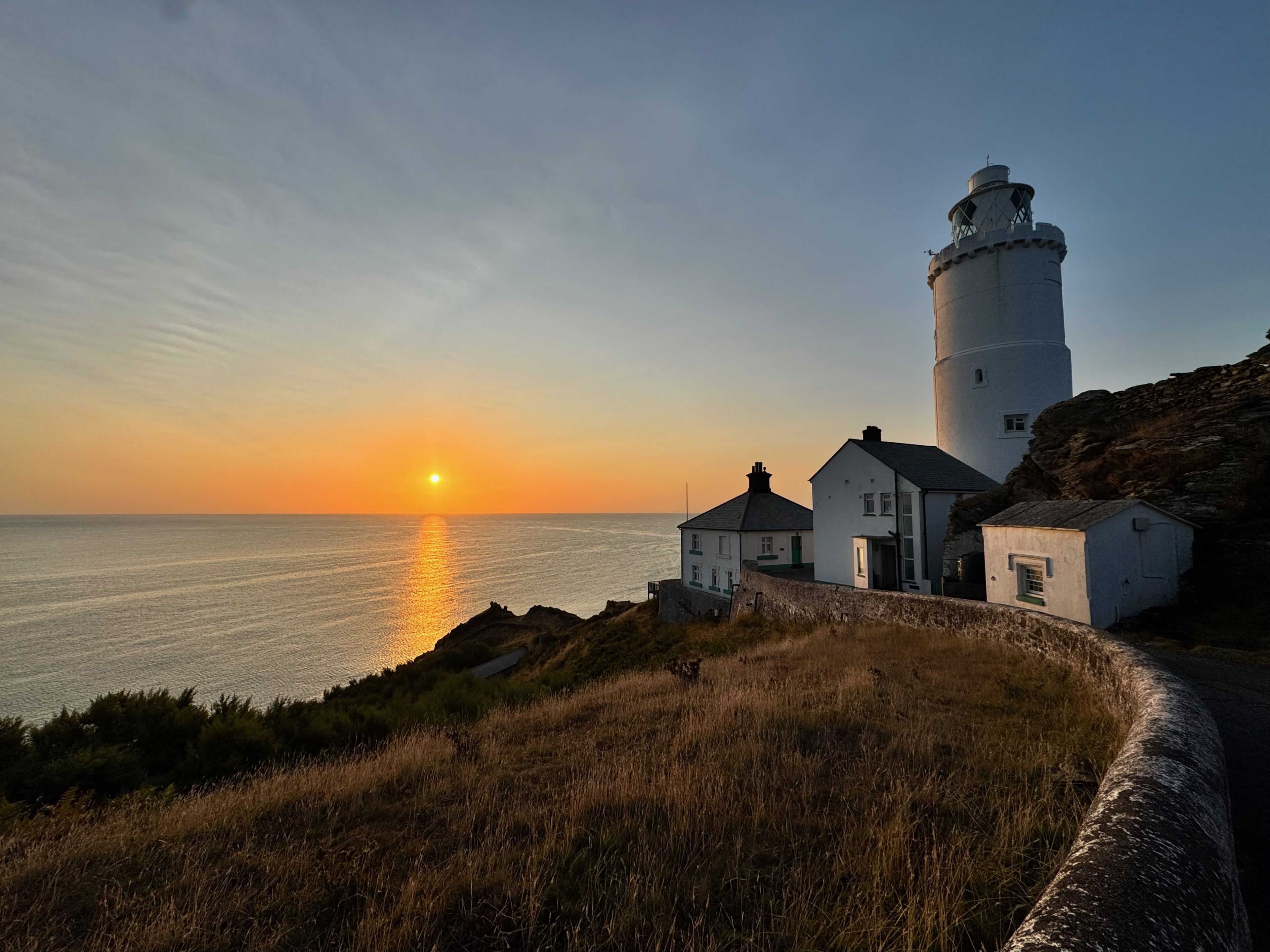 Eine Küstenlandschaft mit einem Leuchtturm, einem kleinen weißen Gebäude und einer Rasenfläche.