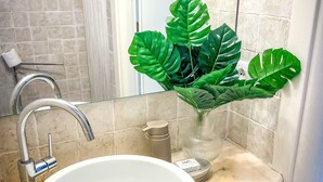 Une salle de bain avec un lavabo blanc, un robinet chromé et une grande plante verte dans un vase en verre.