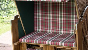 Un banco de madera con cojín de cuadros y asiento a juego, ubicado en un patio de ladrillo.
