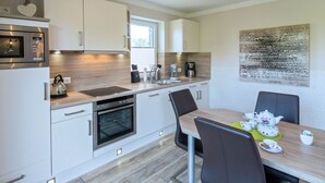Una cocina moderna con armarios blancos, horno empotrado, microondas y cafetera. Hay una mesa de comedor con sillas y un elemento decorativo en la pared superior.