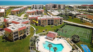 Een resort met meerdere gebouwen, een zwembad, tennisbanen en uitzicht op de oceaan.