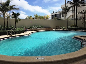 Piscina com indicador de profundidade de 1,8 metros, rodeada por palmeiras e um edifício com design moderno.