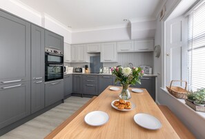 A modern kitchen with grey cabinets, a wooden table, and a vase with flowers.