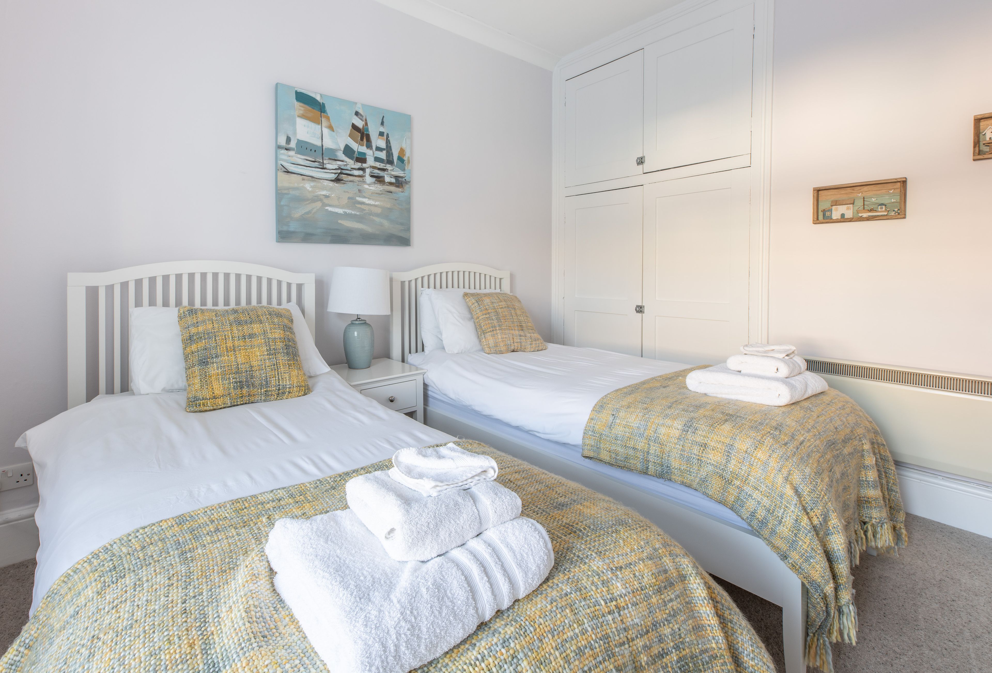 A hotel room with two beds, a painting of sailboats, a wardrobe, and a small framed picture on the wall.