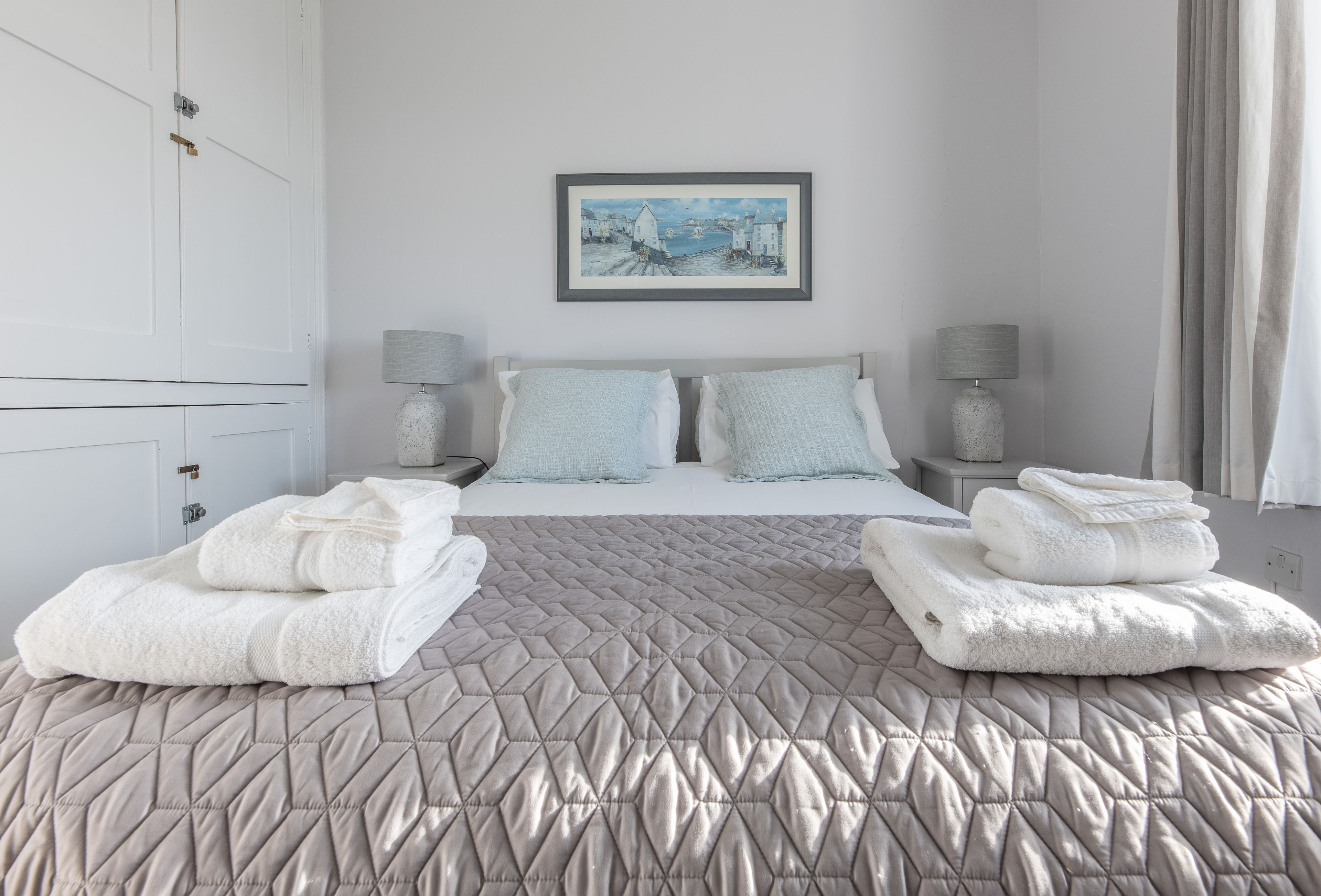 A hotel room with a bed, two nightstands, a painting on the wall, and towels on the bed.